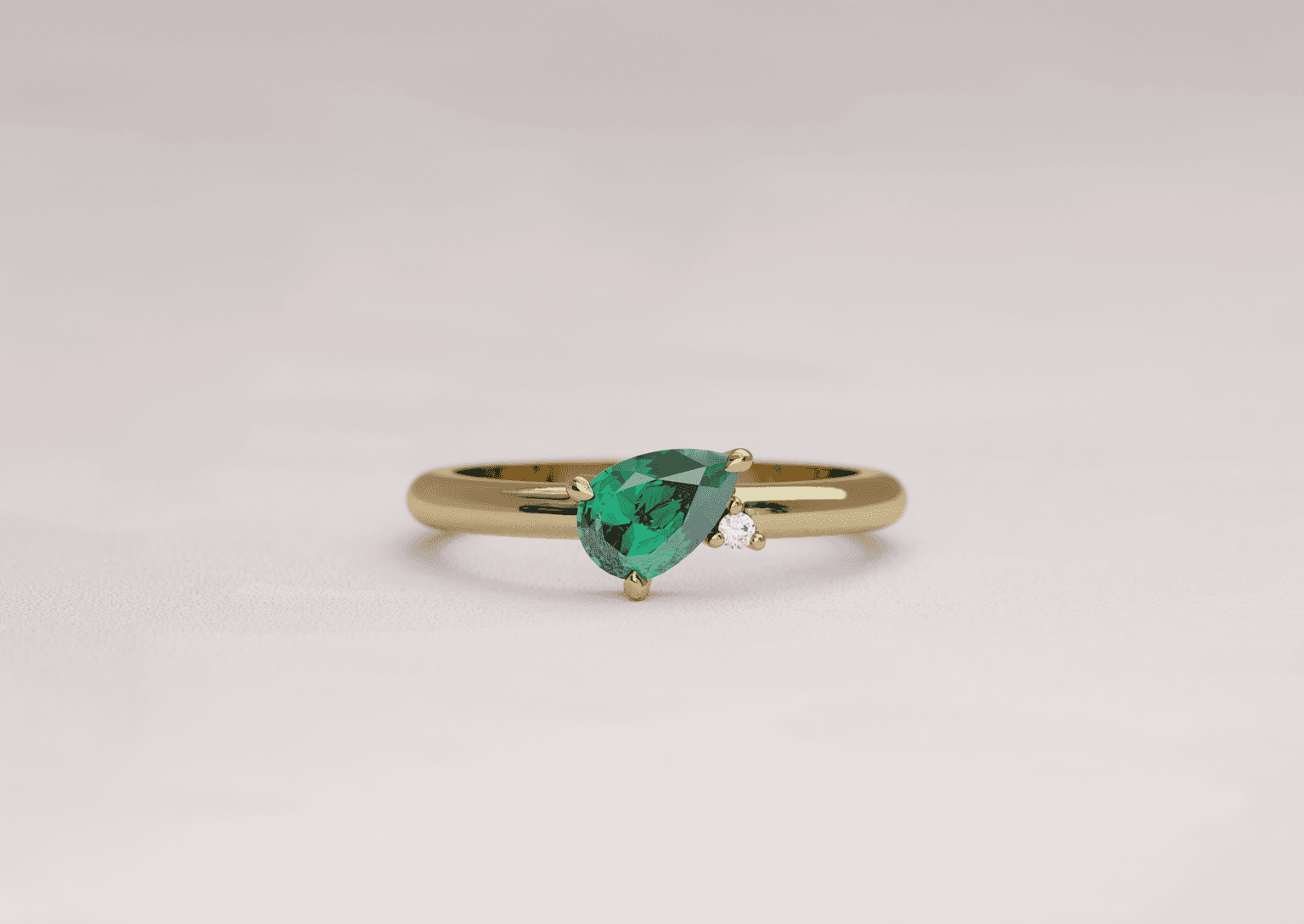 Asymmetric pear cut emerald engagement ring with an accenting round diamond in a yellow gold band