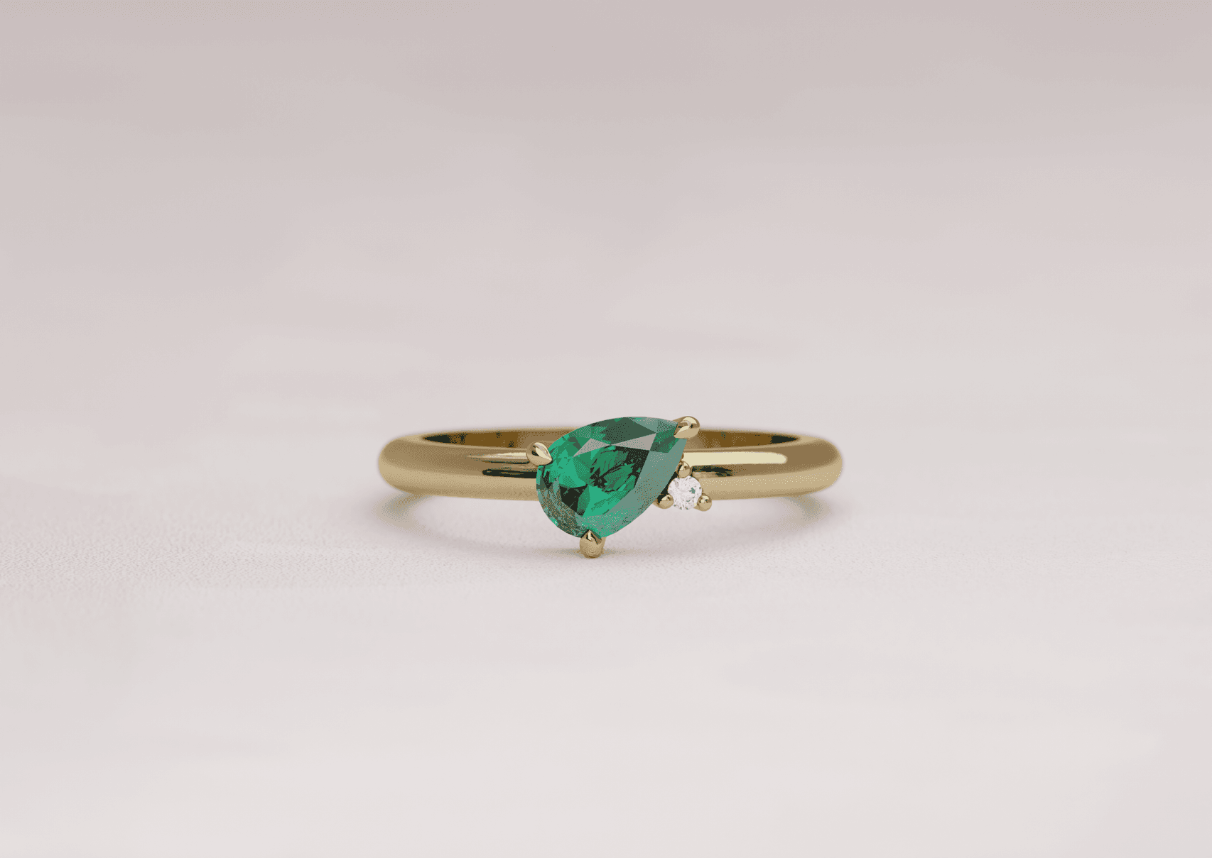 Asymmetric pear cut emerald engagement ring with an accenting round diamond in a yellow gold band