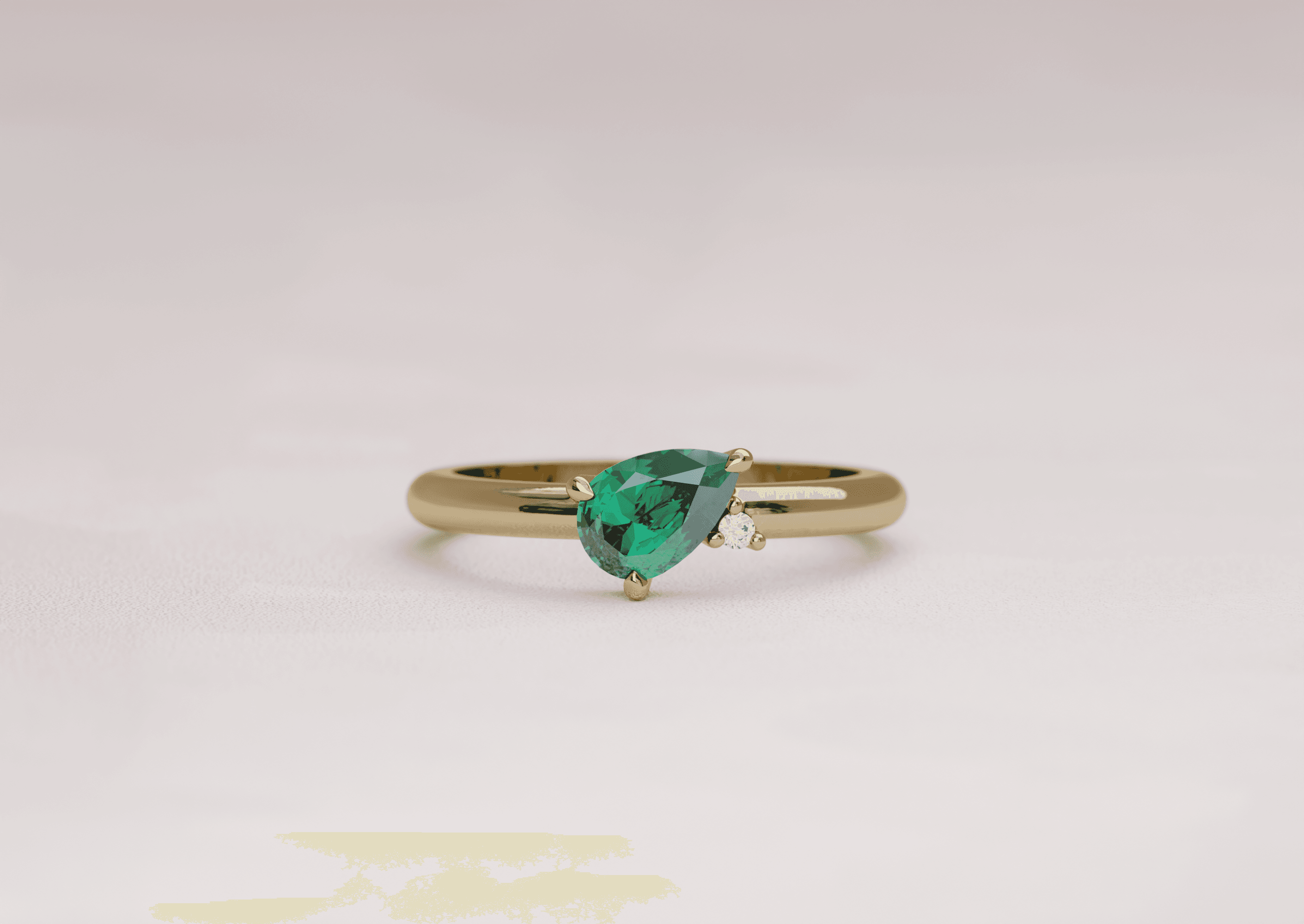 Asymmetric pear cut emerald engagement ring with an accenting round diamond in a yellow gold band