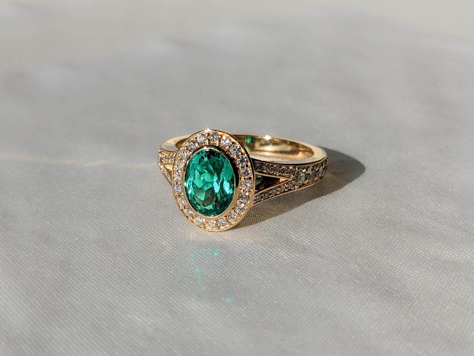 Oval emerald in full bezel with diamond halo with a split shank with diamonds running along the band