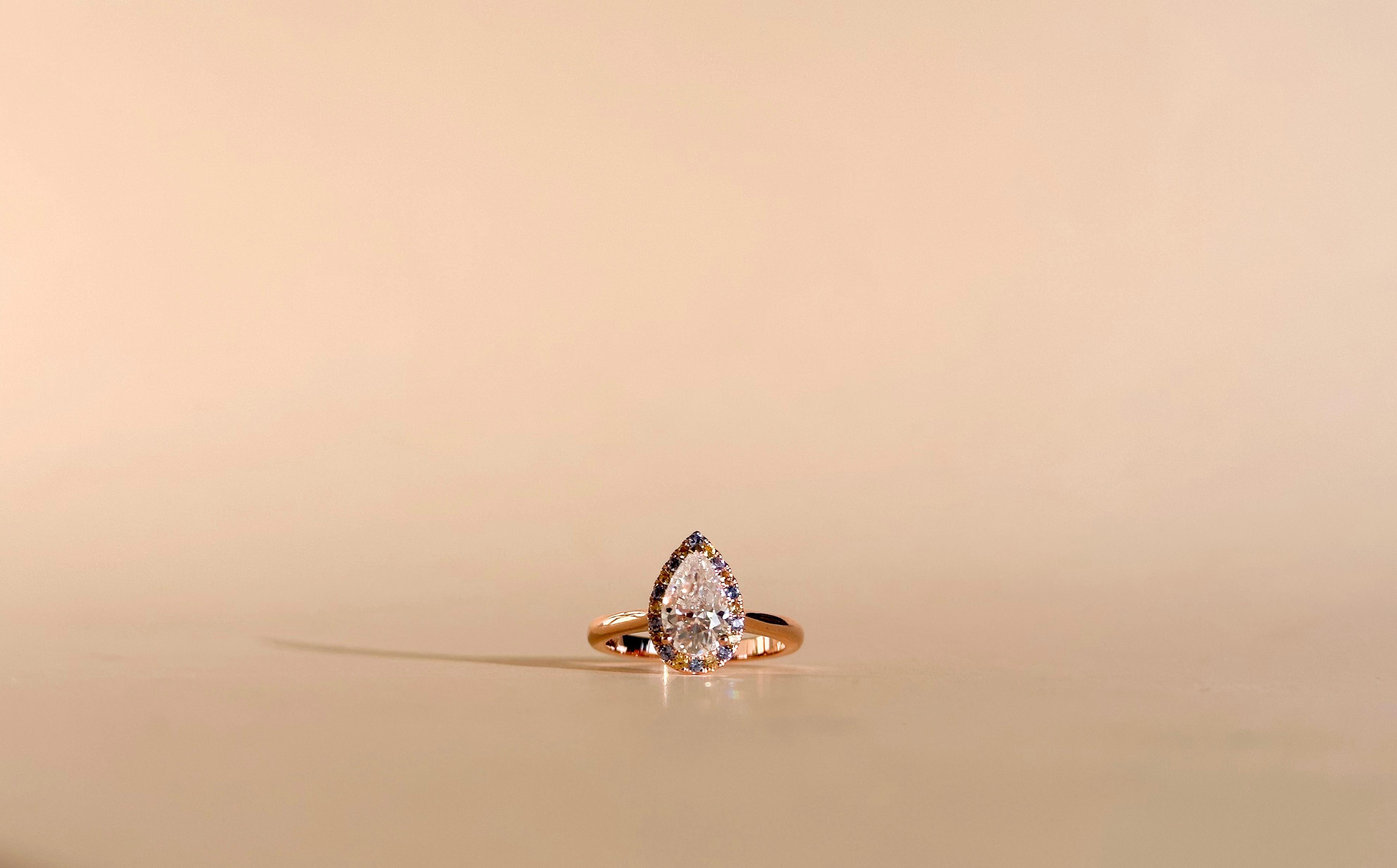 1 carat pear moissanite with different coloured gemstones making up a halo in a 14K yellow gold band