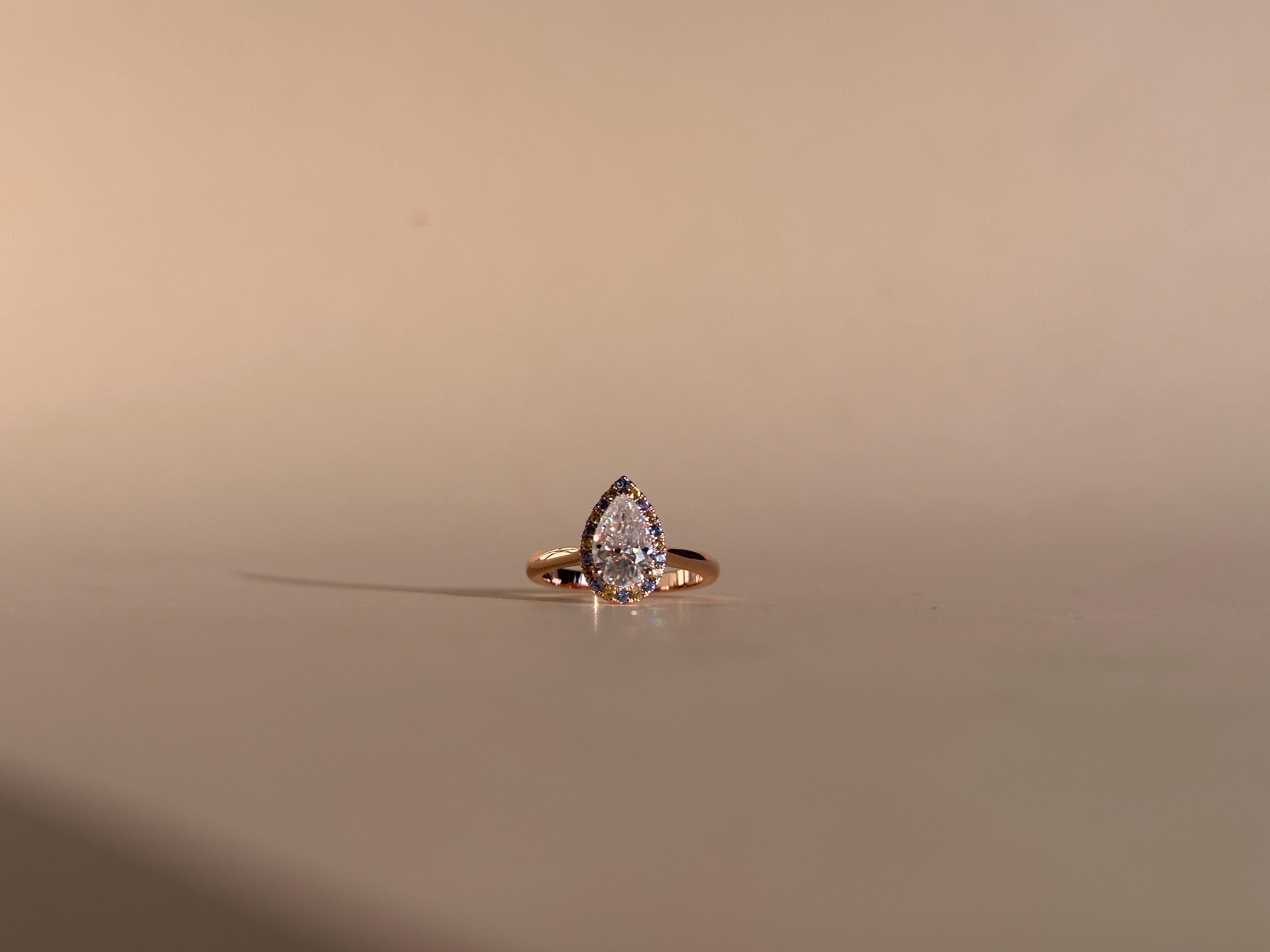 Pear moissanite engagement ring with blue and yellow accenting diamonds on a rose gold ring