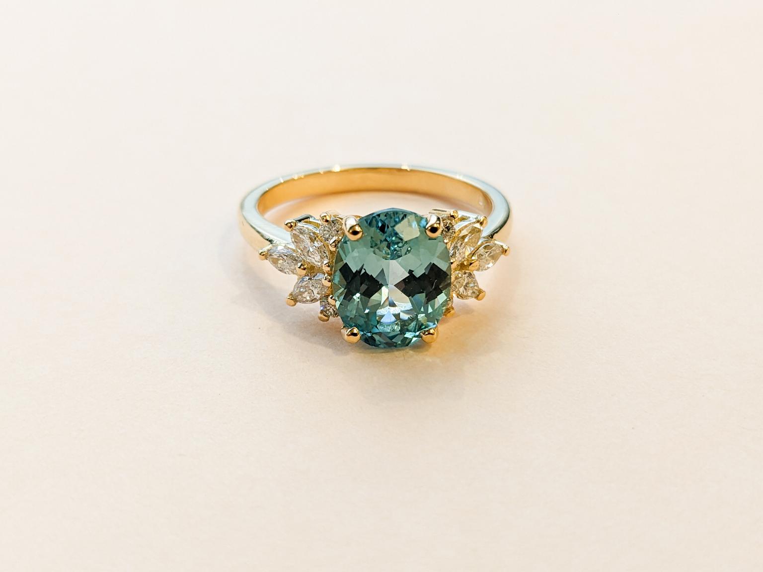 Teal oval sapphire in 10 accenting pear and round diamonds in a yellow gold band