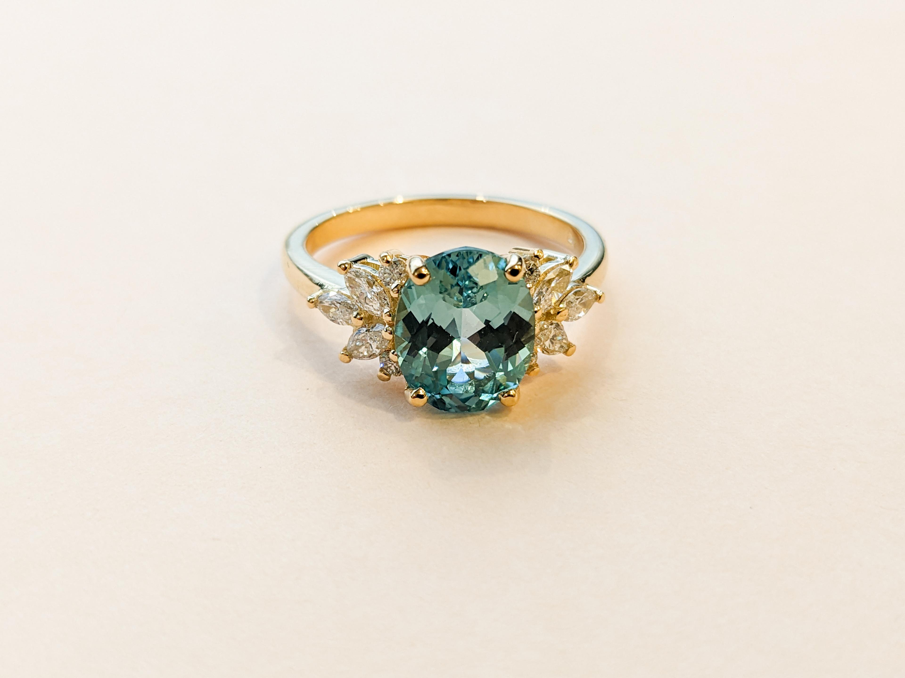 Teal oval sapphire in 10 accenting pear and round diamonds in a yellow gold band