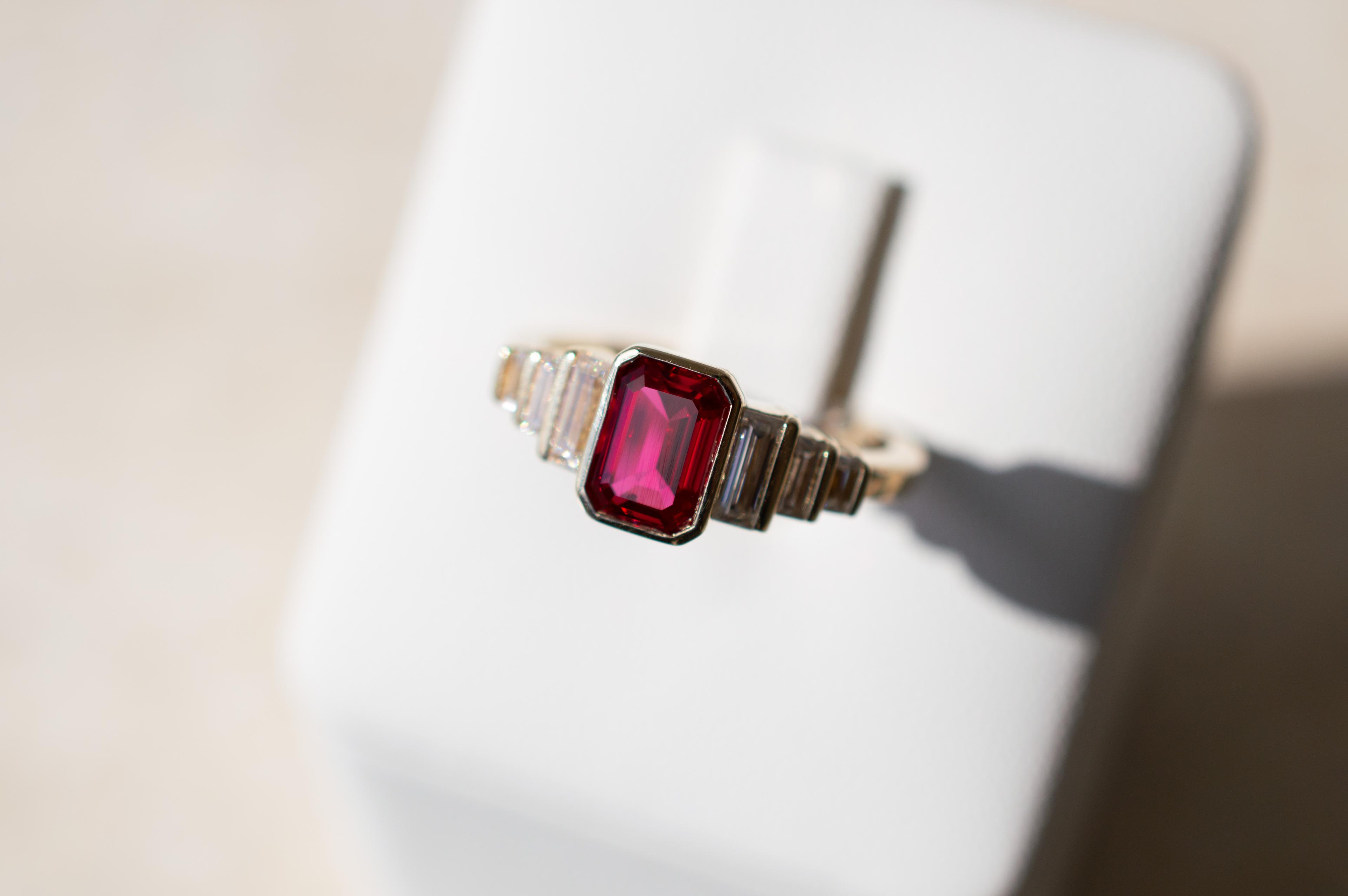 7 stone engagement ring featuring emerald cut ruby and six accenting and descending sized diamonds in a yellow gold band