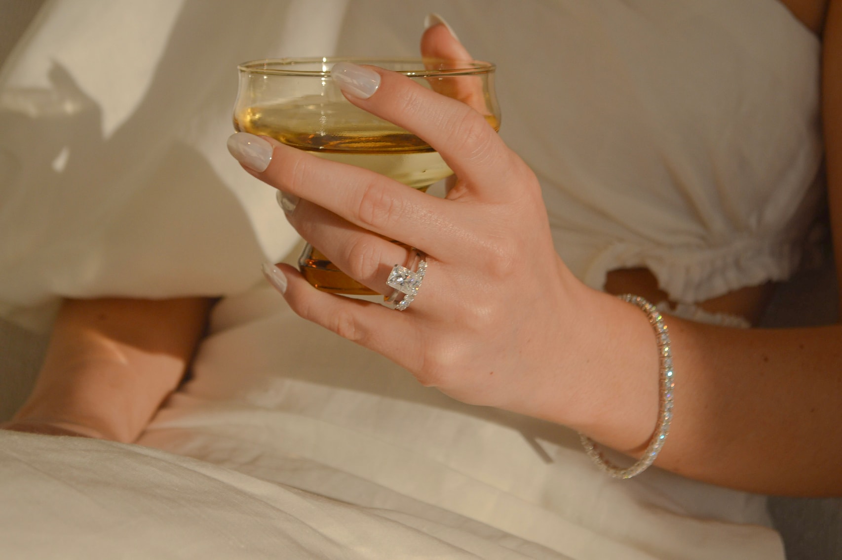 Woman holding a glass showcasing her sustainable jewellery, with flush engagement ring and diamond tennis bracelet